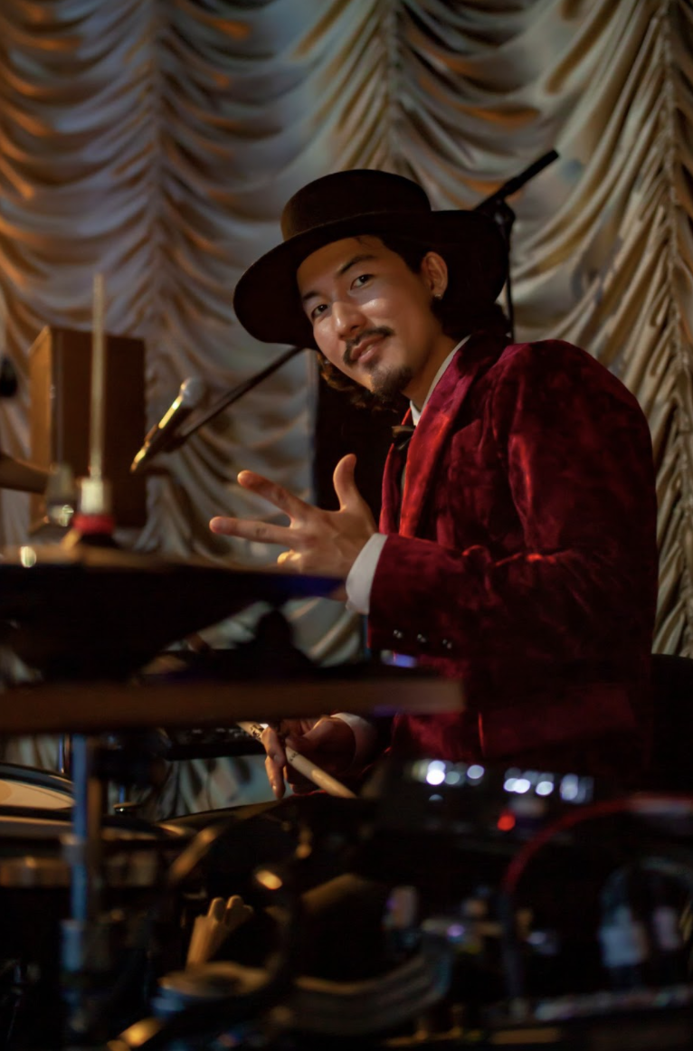 赤い衣装を着てドラムをする神田リョウ