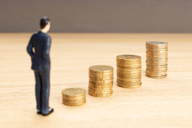 Businessman figurine looking at the growth of a stacked coins. Saving money for finance accounting concept.