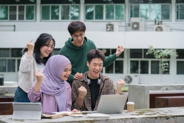 Multi ethnic group of university students raising hands celebration together while looking at laptop screen